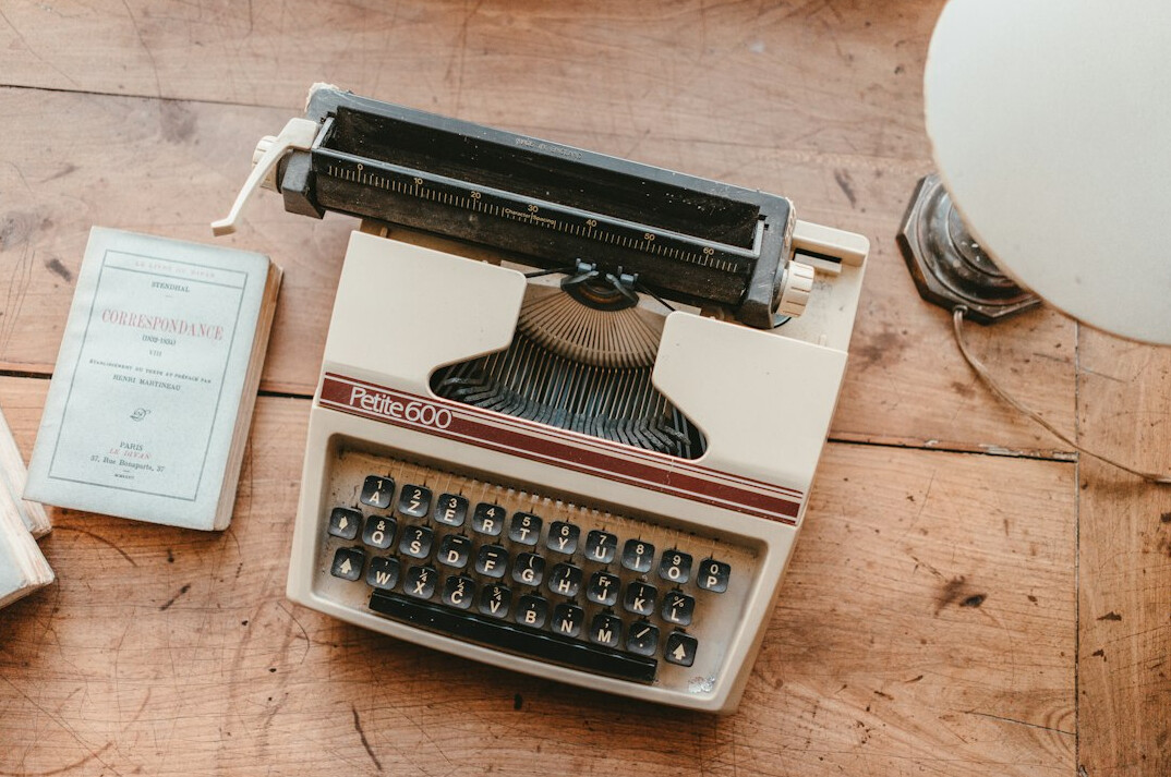 Flat lay of a typewriter, notebook and coffee cup on a wooden desk