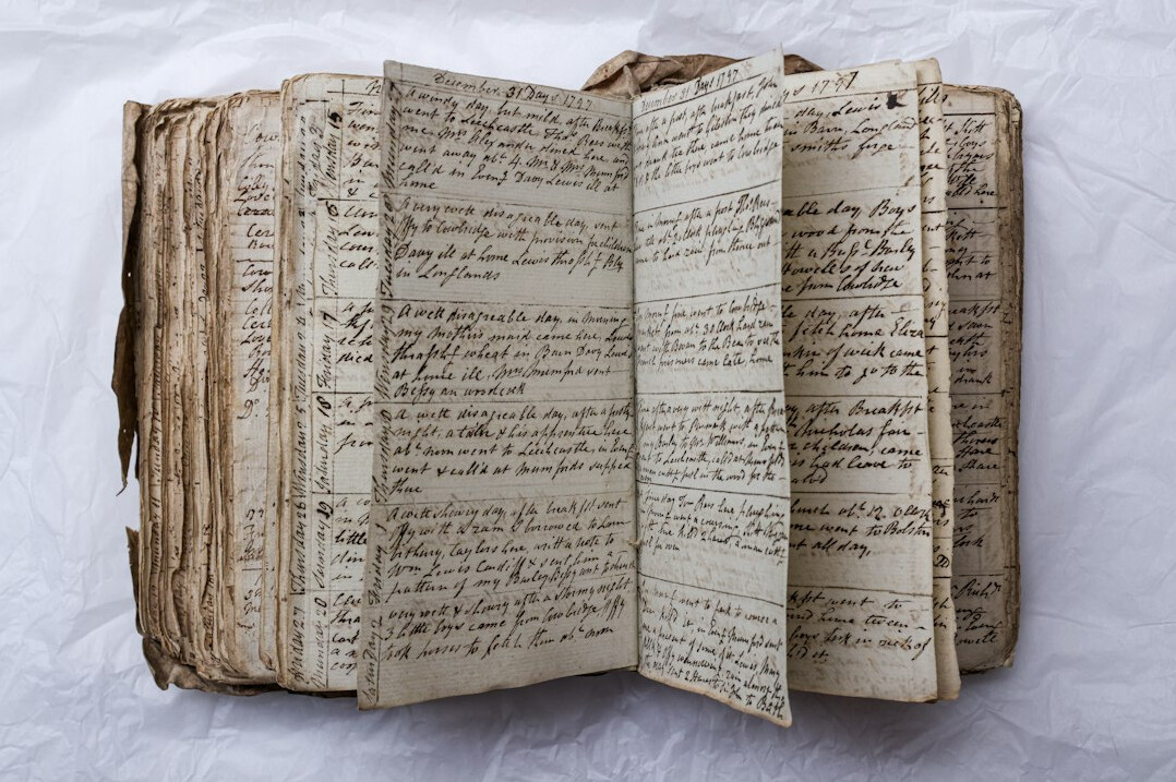 Laptop with manuscript pages and a notebook on a desk at night